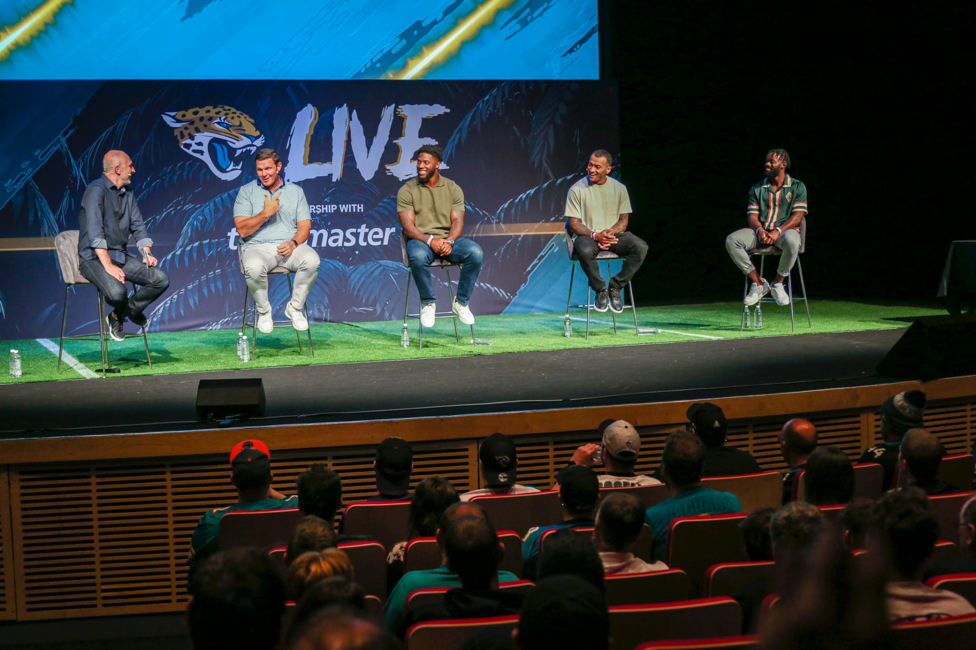 Ayo Oyelola on a live panel discussion stage with a Jacksonville Jaguars backdrop